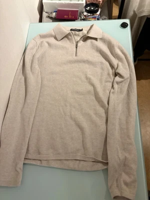 Beige ziptröja från Dressmann - Snygg beige långärmad tröja från Dressmann med krage och halv dragkedja framtill. Tillverkad i mjukt, tunt stickat material som ger en clean och stilren look. Perfekt till jeans eller chinos för en avslappnad vibe.