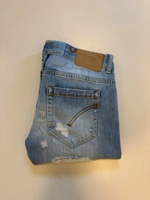 DonDup George jeans - Ljusblåa DonDup jeans med slitningar //  Modell: George slim fit //  Mycket bra skick med fabrik gjorda slitningar som syns på bilderna //  Storlek 30 //  Midja bredd 38cm  Längd 101cm  Innerben längd 78cm  Lårvidd 26cm  Benöppning 15cm  Skriv vid minsta fråga eller fundering🤝 