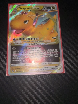 Dragonite VSTAR Pokémonkort - Säljer ett Dragonite VSTAR Pokémonkort med holografisk yta. Kortet har färger i gult, orange och blått, och visar Dragonite med VSTAR Power och attacken Giga Impact. Perfekt för samlare eller Pokémon TCG-spelare.