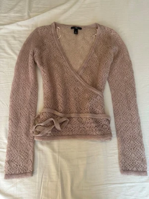 Beige omlottkofta i mohairmix - Supersöt beige stickad omlottkofta från H&M med knytband i midjan. Koftan har ett luftigt spetsstickat mönster och långa ärmar. Materialet känns fluffigt och mjukt, troligen en mohairmix. Perfekt för lager på lager och en chill look.