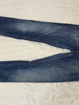 Blå slim fit Acne Jeans - Säljer ett par blå slim fit jeans från Acne med klassisk femficksdesign och snygga slitningar. Jeansen har en något tvättad look och raka ben. Perfekta för dig som gillar stilrena och tidlösa jeans.