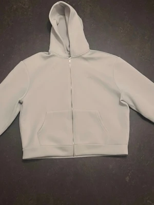 Ljusgrå hoodie från boohooMAN - Snygg ljusgrå hoodie från boohooMAN med dragkedja framtill och stor huva. Hoodien har en klassisk känguruficka och raka, långa ärmar. Perfekt för en chill och stilren look.