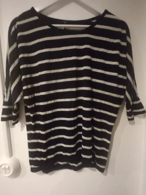 Svartvit randig topp med trekvartsärm - Randig topp i svart och vitt med trekvartsärmar och rund halsringning. Perfekt för dig som gillar en enkel och stilren look. Materialet känns mjukt och lätt, troligen bomull eller polyester. Passformen är normal och toppen är något loose.