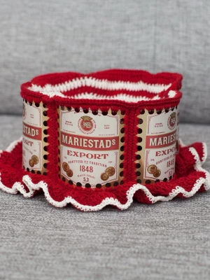 Virkad ölhatt Mariestads  - Unik virkad ölhatt med Mariestads.  Virkad i 100% bomull. Passar upp till 58cm.  Vissa burkar kan ha mindre repor eller bucklor, vilket tyvärr kan uppstå under tillverkningen av hattarna. Insidan av burkarna slipas efter hålen tagits för att undvika vassa kanter. Därför kan det ibland finnas lite slipmärken, men det är inget som stör eftersom det är på insidan av hattarna.  Färger kan variera något beroende på skärminställningar.