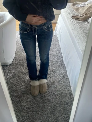Miss me jeans - Säljer ett par mörkblå bootcut jeans från Miss me med snygga slitningar och kontrastsömmar. Jeansen har låg midja, klassiska fickor fram och bak samt detaljerade broderier på bakfickorna. Perfekta för en avslappnad men trendig look.