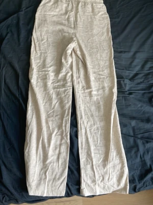Beiga vida linnebyxor med resår - Säljer ett par beiga linnebyxor med breda ben och resår i midjan. Står i storleken XL. Byxorna har en avslappnad passform och är tillverkade i ett lätt och luftigt linnetyg, perfekta för varma dagar. Använd 1 gång