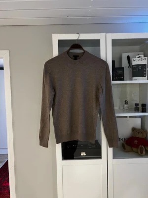 Brun stickad tröja från H&M - Säljer en stilren brun stickad tröja från H&M i regular fit. Tröjan har rund halsringning, långa ärmar och ribbade muddar vid ärmslut och nederkant. Perfekt för lager på lager och enkel att matcha med olika outfits.