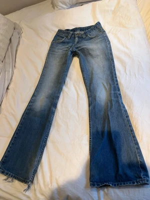 Blå bootcut jeans - Säljer ett par blå bootcut jeans med slitna benslut och snygg tvätt. Jeansen har klassisk femficksmodell, medel midja och är tillverkade i denim. Perfekta för dig som gillar en avslappnad och trendig stil. Jag är 160 som referens!