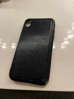 Svart mobilskal i läderlook - Snyggt svart mobilskal med läderkänsla och stilren design. Skalet har öppning för kamera och knappar, passar perfekt för dig som vill ha ett klassiskt och tidlöst utseende på mobilen. Materialet är mjukt men skyddande.