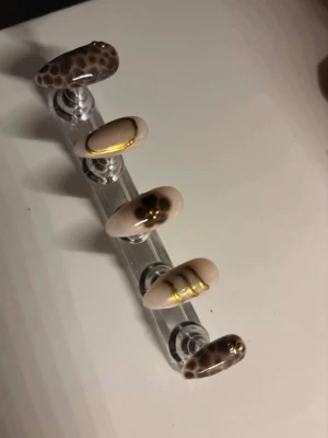 Beige press-on naglar med guld och leopard - Snygga press-on naglar i beige med gulddetaljer och leopardmönster. Mix av mönster: leopard, guldlinjer och en nagel med blomdekor. Mandelformade och trendiga, perfekta för dig som vill ha något unikt. Storlek: M