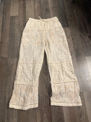 Beige broderade linnebyxor - Säljer ett par beige linnebyxor med broderade detaljer och hålmönster. 
