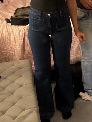 Mörkblå utsvängda jeans med fickor - Snygga mörkblå jeans med utsvängda ben och två stora fickor framtill. Jeansen har hög midja och klassisk knappstängning. De är från bikbok och väldigt populära! Storlek 27/32. Används två gånger!