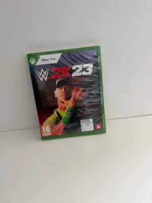 WWE 2K23 Xbox One spel - WWE 2K23 till Xbox One är ett actionfyllt wrestling-spel med realistisk grafik och många olika spellägen. Omslaget har en grön plastbox och spelet är PEGI 16-märkt. Perfekt för dig som gillar wrestling och vill utmana vänner i ringen. Helt ny