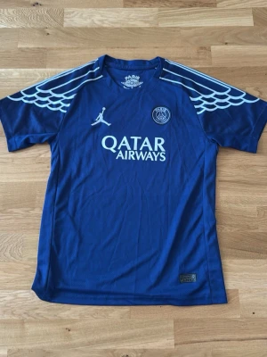 Blå PSG matchtröja Jordan x Nike - Snygg blå PSG matchtröja med vita detaljer och Qatar Airways-tryck på bröstet. Tröjan har det klassiska PSG-emblemet, Jordan-logga och coolt mönster på axlarna. oanvänd, funkar till barn och xs/s kvinna☺️