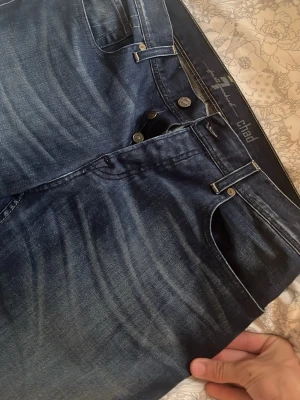 Mörkblå raka jeans från Chad - Snygga mörkblå jeans från Chad med raka ben och klassisk femficksmodell. Jeansen har slitningar och tvättade detaljer för en cool look. Tillverkade i denim med bälteshällor och knappgylf. Perfekta för dig som gillar en avslappnad men stilren stil.