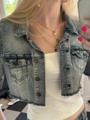 Cropped blå jeansjacka - Trendig cropped jeansjacka i ljusblå tvätt med slitna detaljer och rå kant nertill. Klassisk krage, bröstfickor med knapp och metallknappar framtill. Perfekt för en cool och avslappnad stil.💕💕Är egentligen storlek m men liten i storleken!
