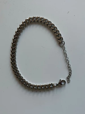 Silverfärgat kedjearmband - Stilrent armband i silverfärgad metall med breda, platta länkar och justerbar kedja. Perfekt för dig som gillar en clean och modern look. Låset är ett klassiskt karbinlås som gör det enkelt att ta på och av.