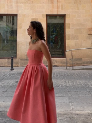 Axelbandslös rosa långklänning - Axelbandslös rosa långklänning med utsvängd kjol och markerad midja. Klänningen har en elegant, enkel design utan mönster och är tillverkad i ett slätt tyg som ger ett exklusivt intryck. Perfekt för dig som vill sticka ut med en feminin och stilren look.