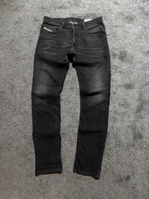 Diesel jeans  - Säljer ett par svarta slim fit jeans från Diesel med snygga slitningar och klassisk femficksdesign. Jeansen har en diskret logga på myntfickan och är tillverkade i mjukt denimtyg med lite stretch för extra komfort.