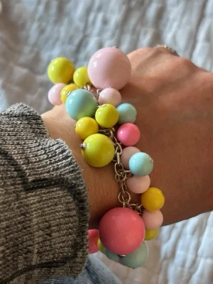 Färgglatt armband med stora pärlor - Säljer ett armband med stora och små pärlor i pastellfärger som rosa, gult, ljusblått och ljusrosa. Pärlorna sitter på en silverfärgad kedja och ger en lekfull och trendig look. Perfekt för dig som gillar färg och vill sticka ut med dina accessoarer.