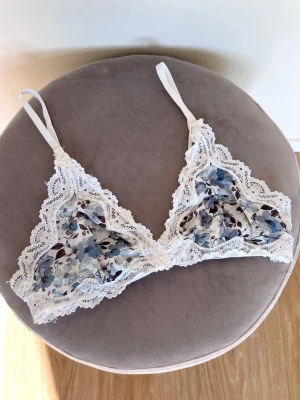 Blommig spets-bralette, Gina Tricot - Säljer en blåblommig tunn bralette med vit spets och inga ilägg. Sparsamt använd. Skulle uppskatta den att vara liten i storleken.