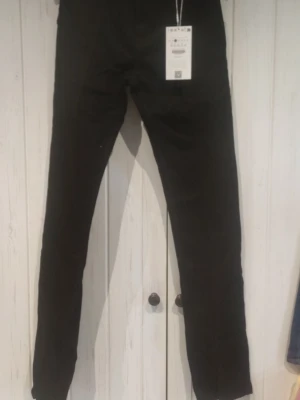 Svarta skinny jeans - Snygga svarta skinny jeans med klassisk femficksdesign och smal passform. Jeansen har en enkel look utan slitningar eller dekorationer, perfekta för en clean och stilren outfit. Materialet ser ut att vara bomullsblandning med lite stretch för extra komfort.