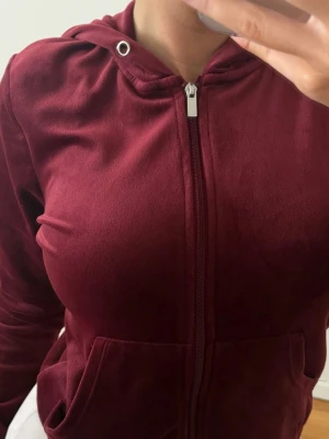 Vinröd kofta från Gina Tricot - Mysig vinröd kofta i mjuk velour med dragkedja framtill och två fickor. Köpt ifrån Gina Tricot. Koftan har en luva där bak. Snören är tyvärr borta så koftan säljes utan snören! Perfekt för en chill och avslappnad stil. Storlek S. Använt några gånger ser bra ut. 