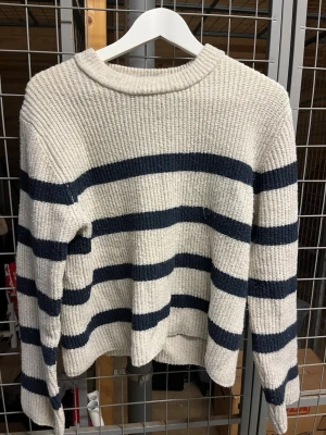 Randig stickad tröja i offwhite och marinblå - Stickad tröja i offwhite med breda marinblå horisontella ränder. Tröjan har rund halsringning, lång ärm och ribbad struktur. Materialet känns mjukt och bekvämt.