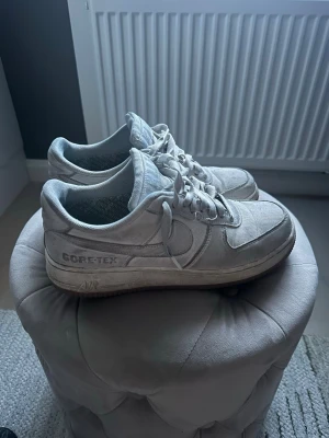 !SÄLLSYNTA! Nike Air Force 1 Gore-Tex vita sneakers  - Nike Air Force 1 sneakers i vitt med Gore-Tex material som gör dem vattenavvisande. Klassisk låg modell med tydlig Nike Swoosh på sidan och AIR-detalj på sulan. Skorna har snörning och robust yttersula för extra grepp. Perfekta för dig som vill ha stilrena och funktionella sneakers.