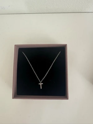 Halsband från Edblad - Snyggt silverfärgat halsband från Edblad med ett T-format hänge dekorerat med små gnistrande diamanter . Kedjan är tunn och elegant, perfekt för dig som gillar stilrena accessoarer med en personlig touch. Kommer i original ask. Helt ny och säljs för att jag har bytt till guld, pris kan diskuteras!🥰