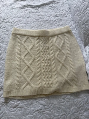 Stickad vit kjol från Gina Tricot - Supersöt stickad vit kjol från Gina Tricot med kabelstickat mönster och ribbad midja. Kjolen är kort och har en mjuk, mysig känsla som passar perfekt till säsongens outfits. Enkel att matcha med både stickade tröjor och boots.