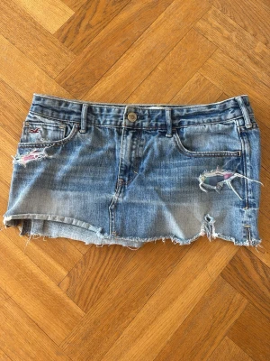 Blå jeanskjol från Hollister - Säljer en blå jeanskjol från Hollister med slitna detaljer och rå kant nertill. Kjolen har klassisk femficksdesign. Skitsnygg jeanskjol som inte kommer till användning!!❤️