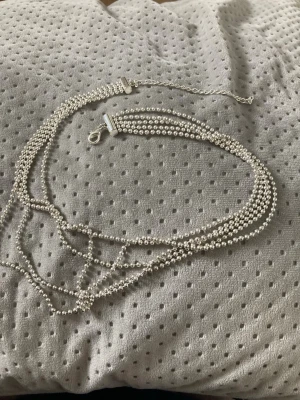 Flersträngat pärlhalsband i silver - Säljer ett flersträngat halsband med små, silverfärgade pärlor. Halsbandet har flera tunna rader av pärlor som ger en cool lager-på-lager-effekt. Låset är i silver och har en enkel karbinhake. Perfekt för dig som gillar stilrena accessoarer med lite extra detalj.