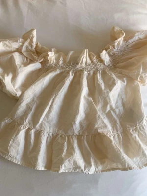 Offshoulder blus från Gina Tricot💓💓 - Söt offshoulder blus från Gina Tricot i ljusbeige. Blusen har puffiga korta ärmar, smockdetaljer upptill och volangkant nedtill. Den är ganska kort, den är i storlek xs💓