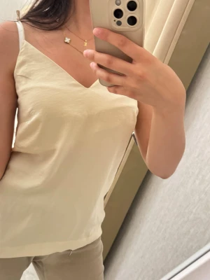 Beige linnetopp med v-ringning - Snygg beige linnetopp med v-ringning och smala axelband. Perfekt för varma dagar och enkel att styla med olika accessoarer. Tidlös och stilren design som passar till det mesta.