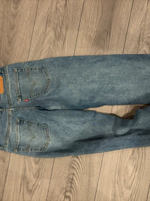 Levi's ljusblå loose taper  - Säljer ett par klassiska ljusblå Levi's jeans med raka ben och femficksmodell. Jeansen har den ikoniska röda Levi's-lappen på bakfickan och är tillverkade i slitstark denim. Perfekta för en avslappnad och trendig look. Byxorna är lite mer åt baggy hållet och bootcut