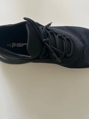 Svarta sneakers från Sneakers Point - Stilrena helsvarta sneakers från Sneakers Point med låg profil och klassisk snörning. Ovandelen är i mesh-liknande material för bra andningsförmåga och skon har en mjuk, bekväm sula. Perfekta för dig som gillar en clean och sportig look.