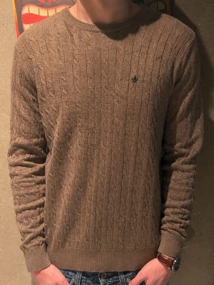 Stickad Morris tröja - Snygg brun kabelstickad tröja från Morris med rund halsringning och diskret broderad logga på bröstet. Perfekt för lager-på-lager. Modellen är 185cm cirka