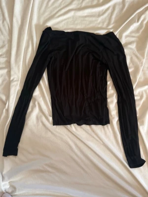 Svart offshoulder topp med lång ärm - Trendig svart offshoulder topp med långa ärmar och en snygg öppen rygg. Tunn och stretchig, perfekt att styla till olika looks. Materialet känns mjukt och följsamt mot huden.