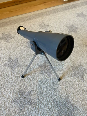 Grå teleskop med stativ - Säljer ett grått teleskop i metall med justerbart stativ i silver. Perfekt för att utforska natthimlen eller spana på avlägsna objekt. Kompakt design som gör det enkelt att flytta runt och använda både inomhus och utomhus.