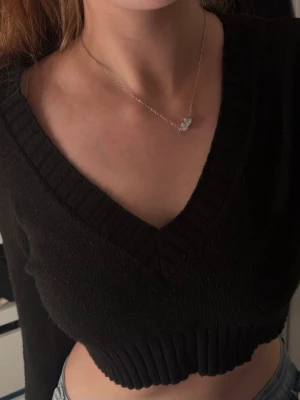 Svart croppad stickad tröja - Snygg svart croppad stickad tröja med djup V-ringning och bred ribbad kant nedtill. Perfekt att matcha med höga jeans eller kjol för en trendig look. Mjuk och skön kvalitet som känns lyxig mot huden.