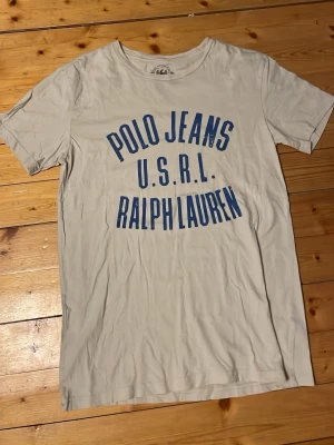 Vit Polo Jeans t-shirt från Ralph Lauren - Vit t-shirt från Polo Jeans Ralph Lauren med blå tryckt text på bröstet. Klassisk rund halsringning och korta ärmar. Tillverkad i mjuk bomull som känns skön mot huden. Perfekt för en avslappnad och stilren look. Storlek S i toppskick priset går att diskutera!