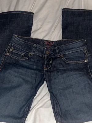 lowwaist jeans från Guess med broderi på fickorna - Snygga mörkblå jeans från Guess med klassisk femficksmodell och dekorativa broderier på bakfickorna. Jeansen har låg midja och är bootcut. Perfekta för dig som gillar en stilren men ändå detaljerad look.