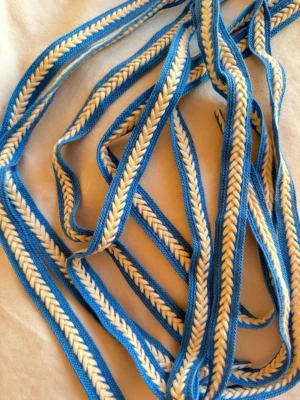 Blått och vitt flätat tygskärp - Säljer ett unikt flätat tygskärp i blått och vitt. Skärpet har en snygg fiskbensmönstrad design och är tillverkat i mjukt textilmaterial. Perfekt för att ge din outfit en färgklick och en personlig touch. Skosnöre!