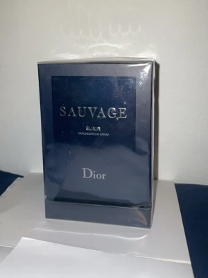 Dior Sauvage Elixir parfym - Dior Sauvage Elixir är en exklusiv herrparfym i en elegant, mörkblå glasflaska med silverfärgad text. Flaskan har en rund, robust form och ett stilrent svart lock. Förpackningen är också mörkblå med tydlig Dior-logga. Perfekt för dig som gillar lyxiga dofter.