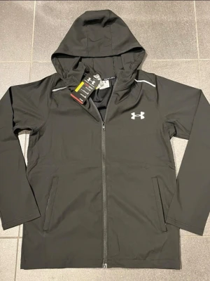 Under Armour vindjacka - lätt, bekväm och perfekt för både träning och vardagsbruk. Skyddar mot vind och passar bra med en sportig stil. I gott skick. Pris kan diskuteras vid snabb affär.