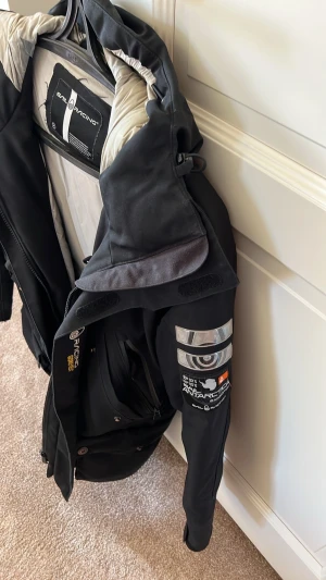 Svart parkas Sail Racing herr - Säljer en svart parkas från Sail Racing med grått innerfoder och coola detaljer som tryck och patchar på ärmarna. Jackan har flera fickor med dragkedja och knappstängning, samt en rejäl huva. Perfekt för kalla dagar och riktigt snygg streetstil.