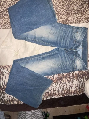 Blå flared jeans från Cheap Monday - Säljer ett par blå bootcut jeans från Cheap Monday med snygg slitning på framsidan. Storlek 28/32. Jeansen har klassisk femficksmodell, dragkedja och knapp i guld. Tillverkade i bomull med en skön passform och retrovibbar. Lite som sticker ut på baksida se på bild 4