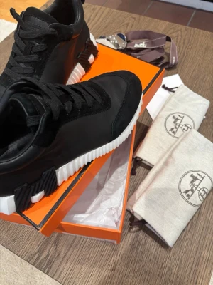 Märkes skor  - Snygga svarta märkes sneakers med chunky vit sula och svarta detaljer på sidan. Skorna har en modern design med blandning av läder och textil, samt svarta skosnören. Perfekta för dig som gillar exklusiva och trendiga sneakers.