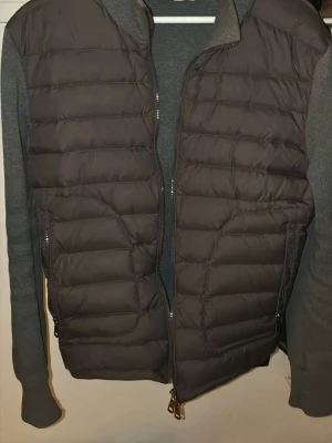 Grå Moncler cardiganjacka - Snygg grå cardiganjacka från Moncler med quiltad front och stickade ärmar. Jackan har dragkedja framtill och Moncler-logga på ena ärmen med NFC tagg. Inristad moncler logga på dragkedjan. Perfekt cardigan för vår/höst.